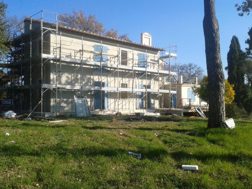 Villa a due piani avvolta dai ponteggi, con prato in primo piano